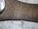 Close-up of the textured dark brown leather strap near the case, showing stitch detail and minor wear.