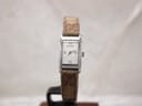 Front view of Gucci 8600L ladies' watch on a display stand, showing the silver rectangular dial with Roman numerals and brown fabric strap.