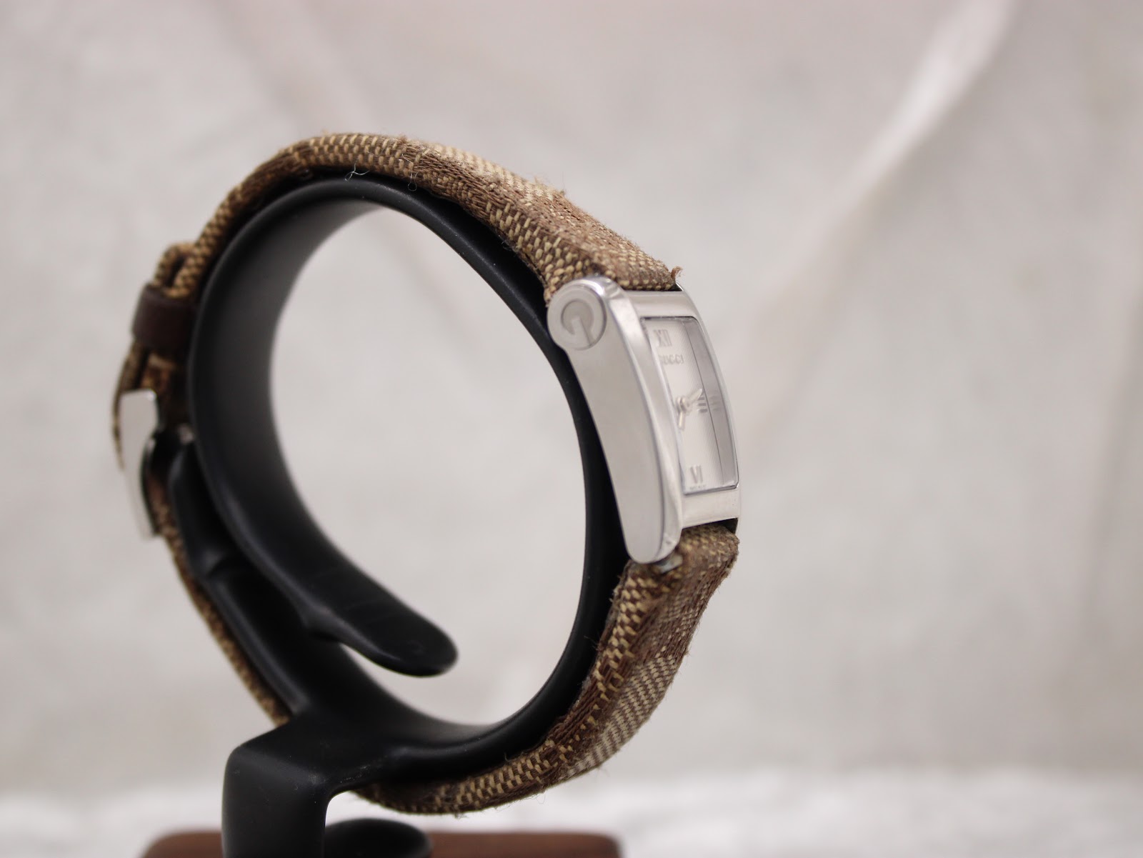 Left-side profile view of the Gucci 8600L watch on a stand, showing the slim rectangular case and strap attachment.