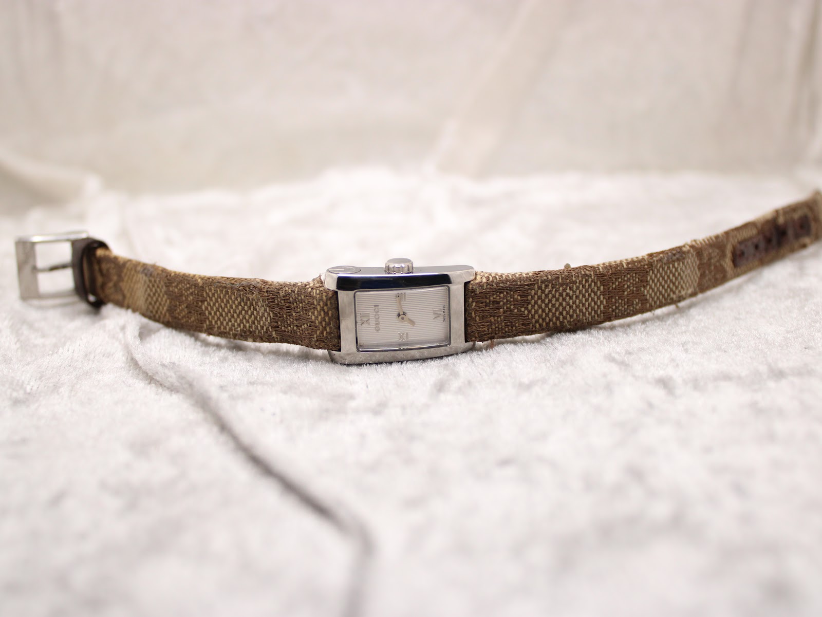 Front view of the Gucci 8600L watch with the fabric strap laid flat on a white textured surface, showing the full length.