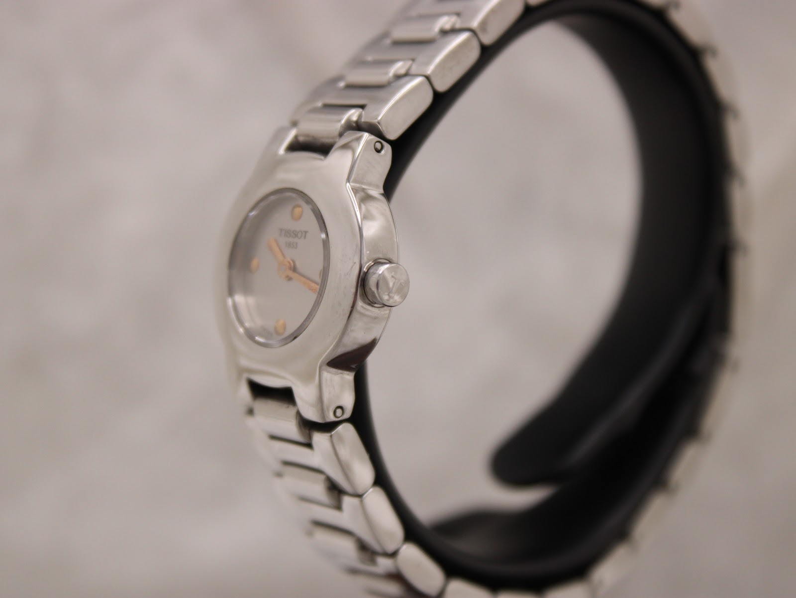 Angled side view of the Tissot watch on a display stand, highlighting the case and crown.