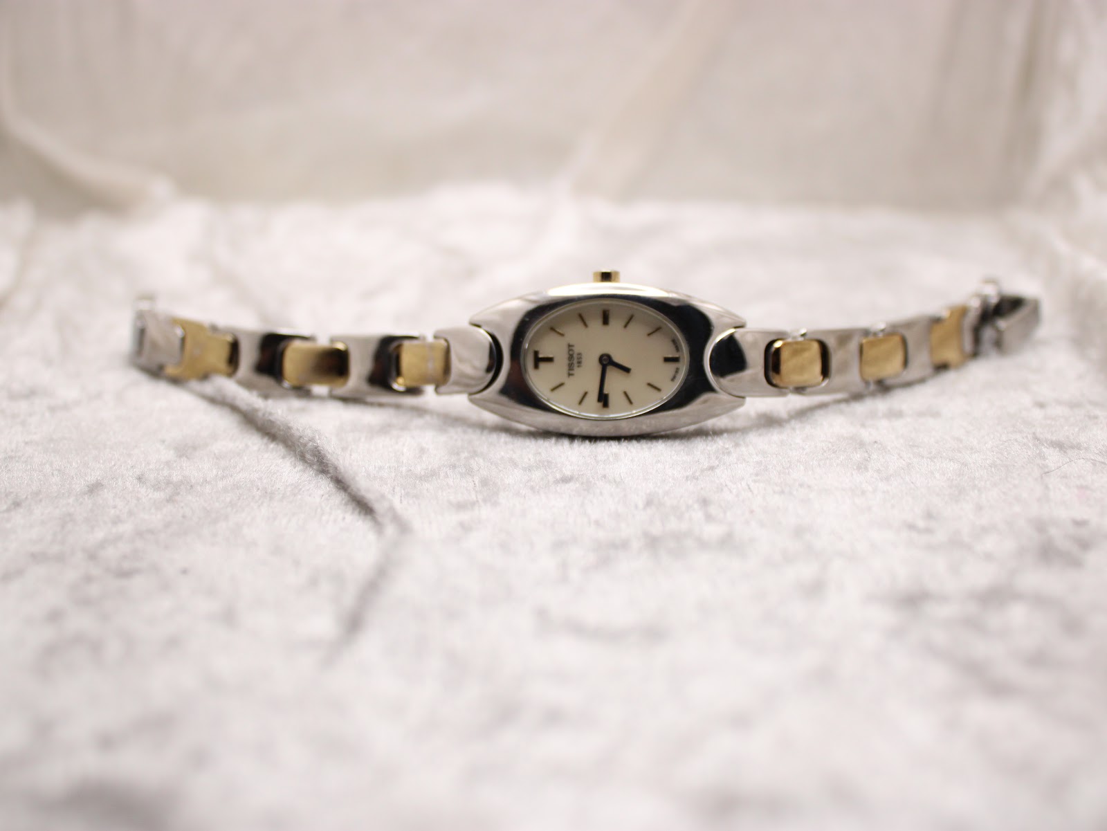 Full view of the Tissot G350 two-tone bracelet and oval watch head laid flat on a textured white surface.
