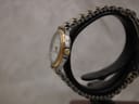 Side profile of the Tissot Seastar watch displayed on a black stand, highlighting the gold-tone crown and the curvature of the case.