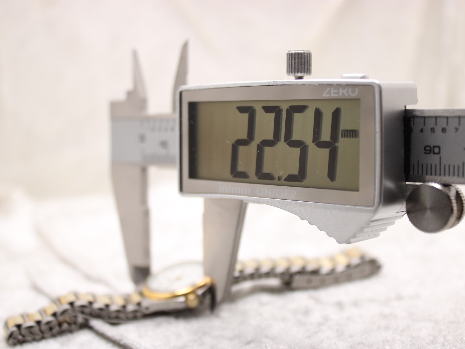 A digital caliper measuring the watch case diameter, displaying an exact measurement of 22.54 mm on the screen.