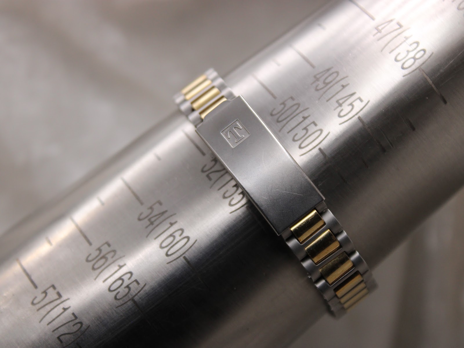 The watch bracelet wrapped around a metal sizing gauge, indicating a maximum wrist circumference fit of approximately 155mm.