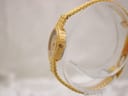 Side profile view of the Tissot ladies' watch, showing its slim gold-tone case, decorative bezel, and fluted crown on a clear stand.