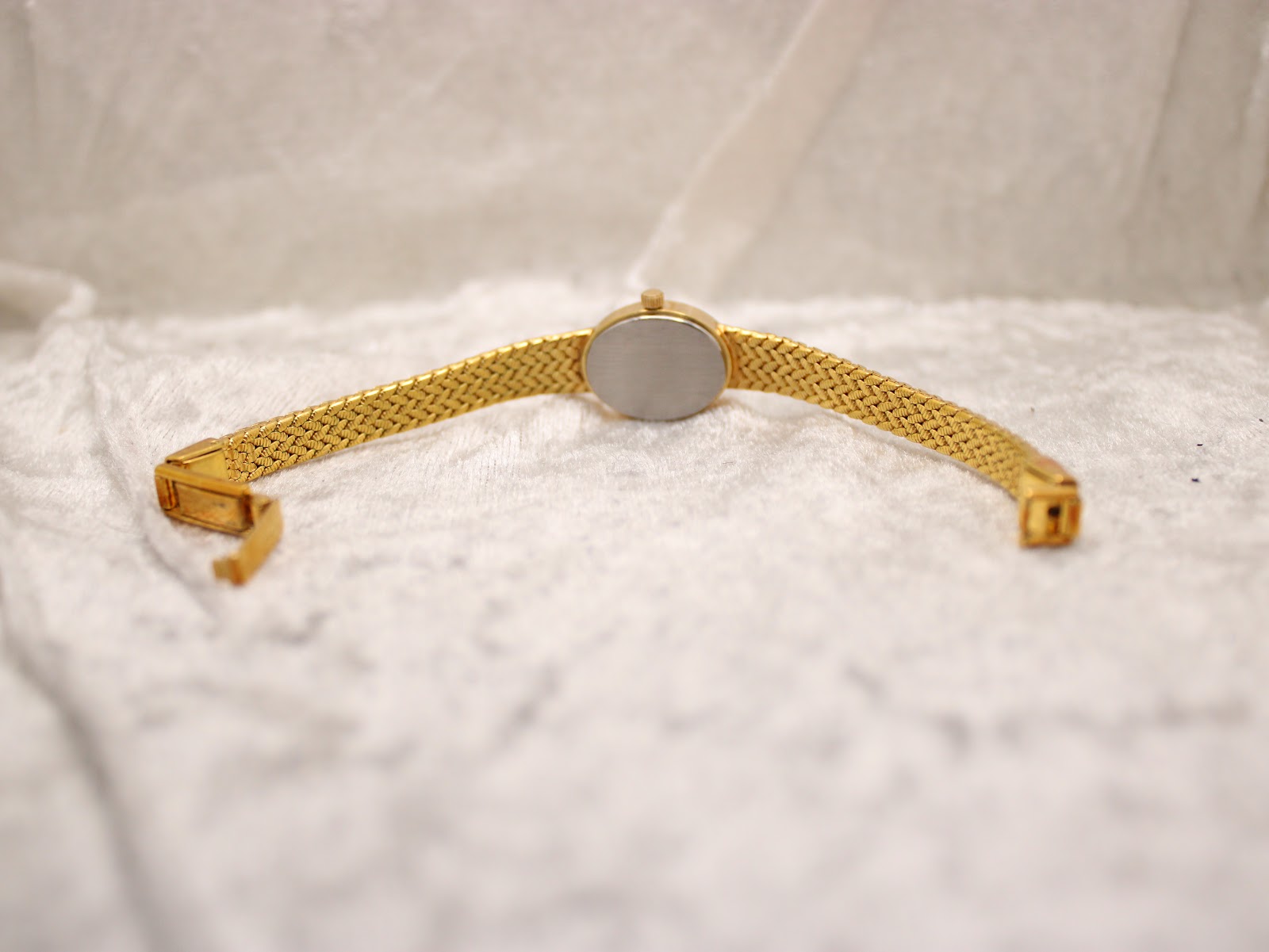 Rear view of the Tissot ladies' watch, showing the brushed stainless steel case back and the unclasped gold-tone woven bracelet.