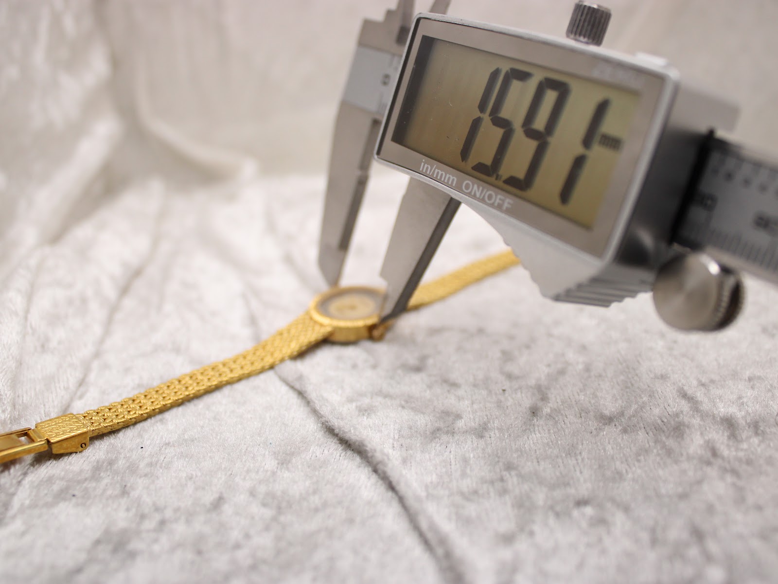 Digital caliper measuring the width of the Tissot watch case, showing a precise measurement of 15.91mm.