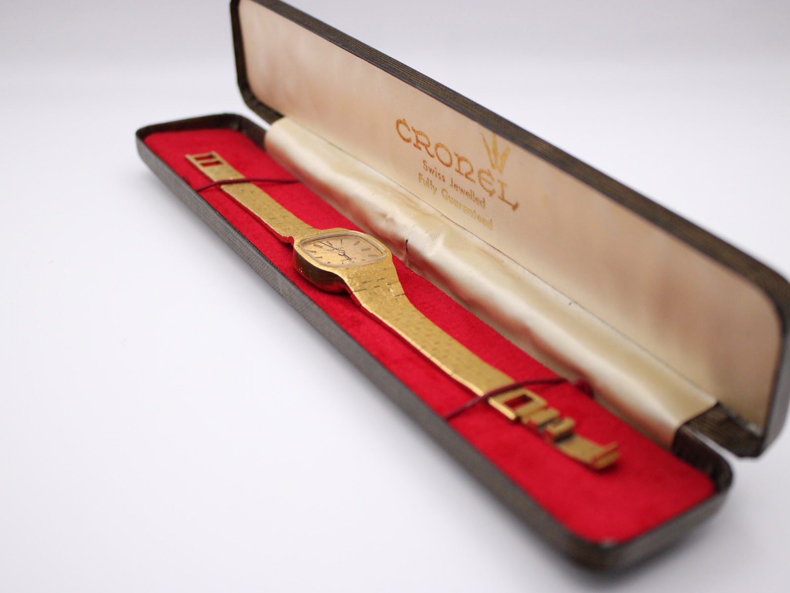 The vintage Tissot watch resting inside an open, contrasting Cronel-branded presentation box with red velvet lining and a cream silk interior.