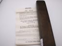 Close-up of a folded white guarantee document with vintage script, positioned next to the dark brown watch box.