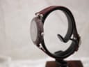 Side profile view of the Tissot RockWatch on a stand, showcasing its slim design and the natural texture of the burgundy stone case.