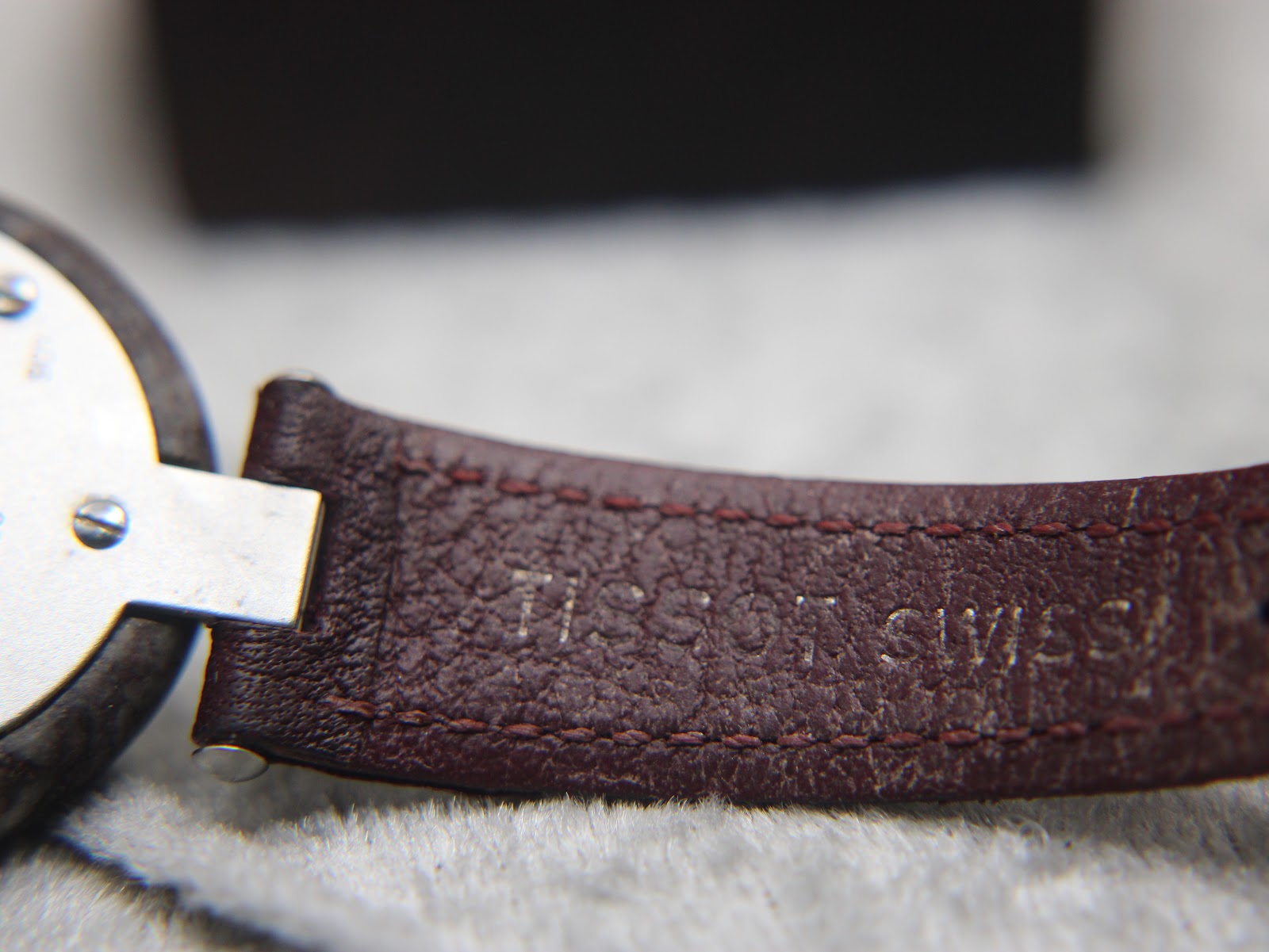 Close-up of the burgundy leather strap, showing its textured finish and embossed 'TISSOT SWISS' text.