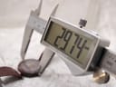 Close-up of a digital caliper measuring the watch case diameter, with the display showing 29.74 mm.