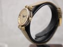 Side view of the Gucci 2000L watch, showing the slim gold-plated case and signed crown, on a black stand.