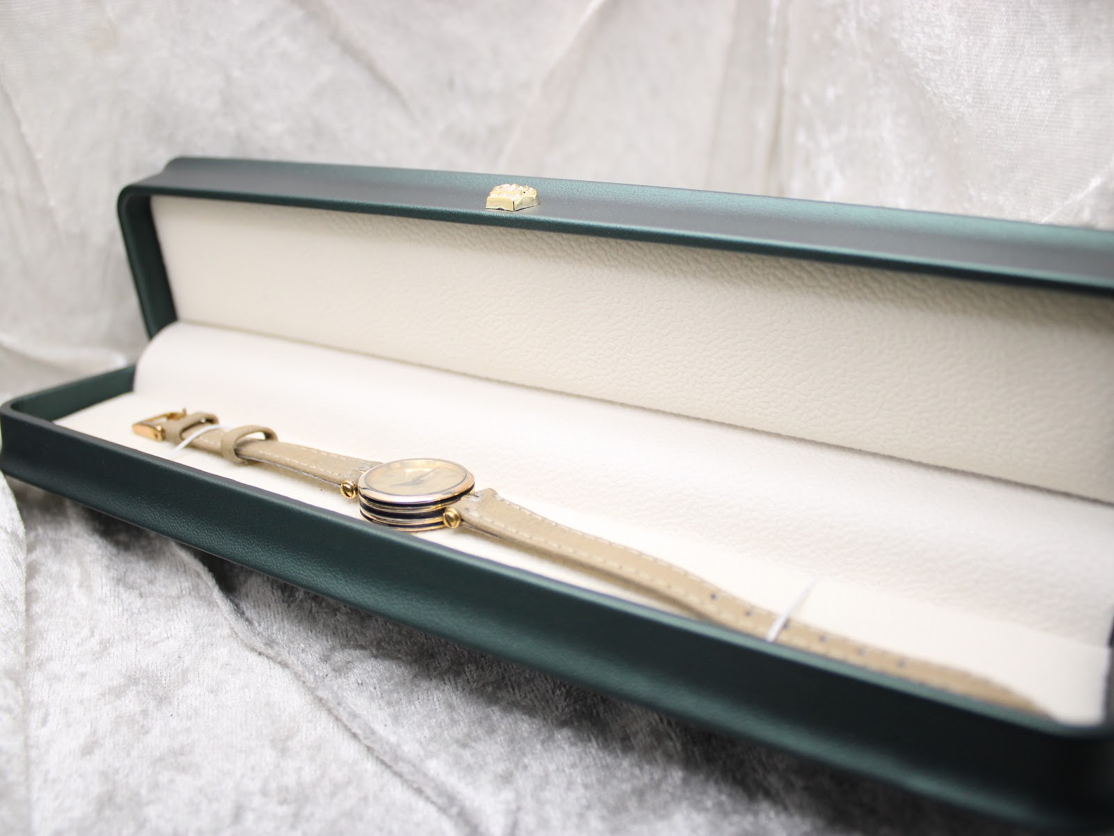 The Gucci 2000L watch with its beige leather strap presented in an open green watch box, on a white textured surface.