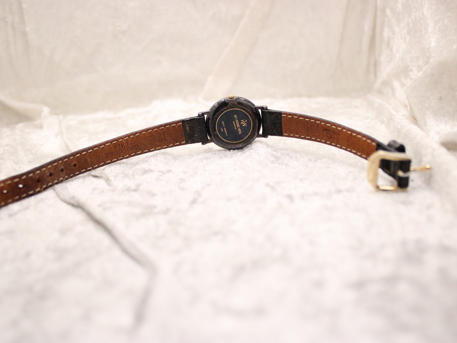 Rear view of the Raymond Weil Othello watch, showing the worn black leather strap and the case back on a soft white surface.