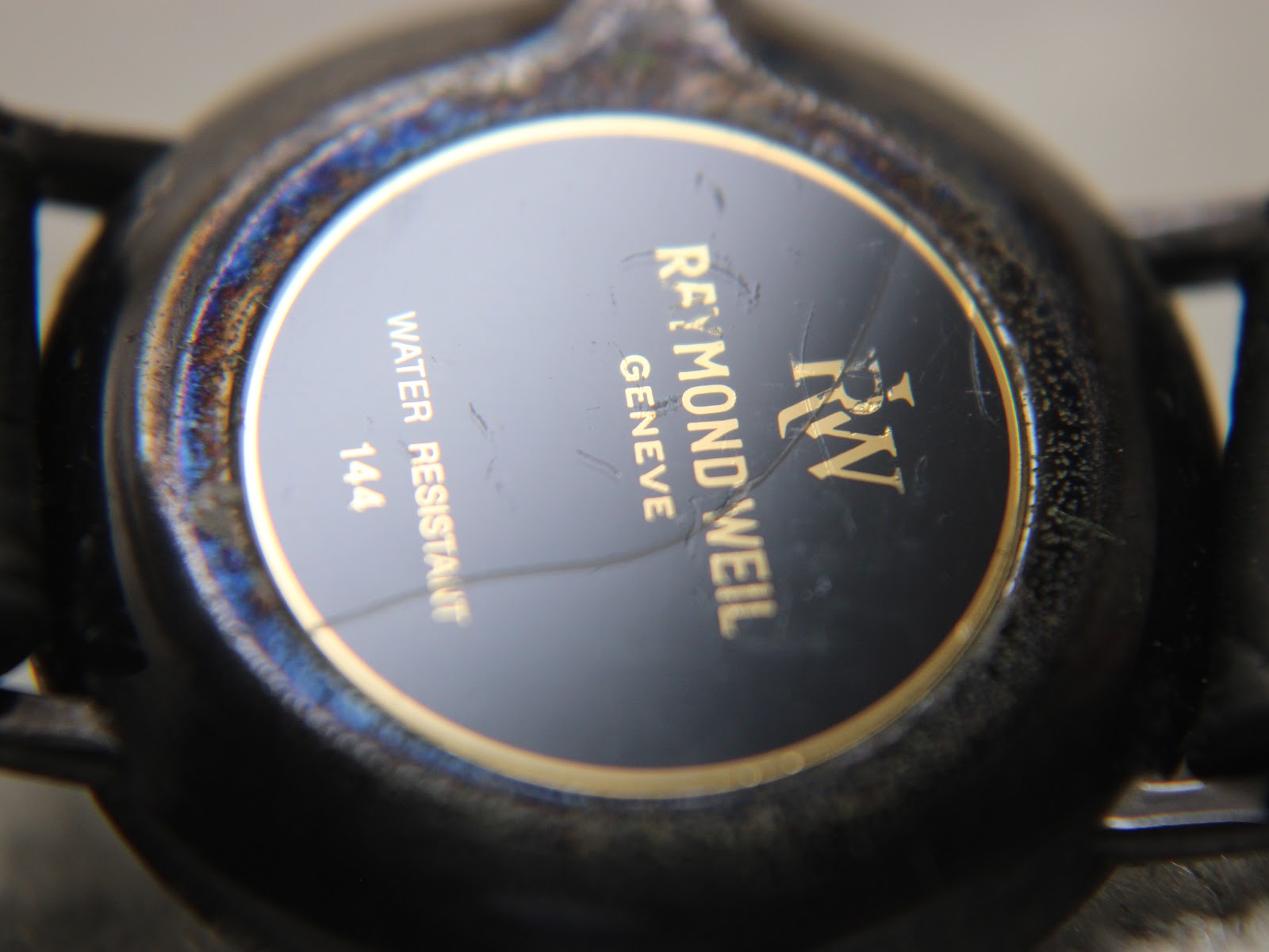 Close-up of the watch case back, engraved with "Raymond Weil Genève" logo, "Water Resistant", and "144", showing some cosmetic wear and a metallic sheen.