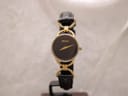 Front view of the Gucci 6000.2 L watch, featuring a black dial, gold-tone case, and black leather strap on a watch stand.