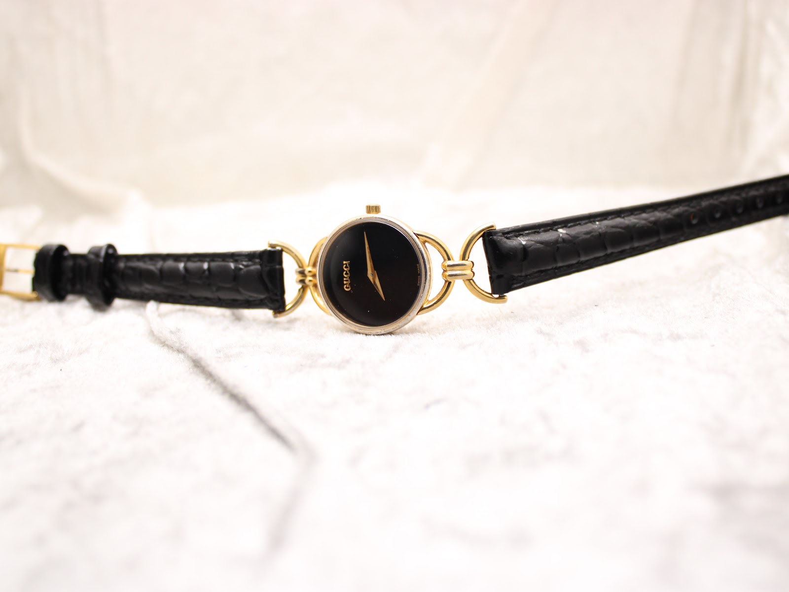 Overhead view of the Gucci watch laid flat, displaying the black leather strap and gold-tone case with its minimalist black dial.