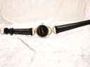 Overhead view of the Gucci watch laid flat, displaying the black leather strap and gold-tone case with its minimalist black dial.