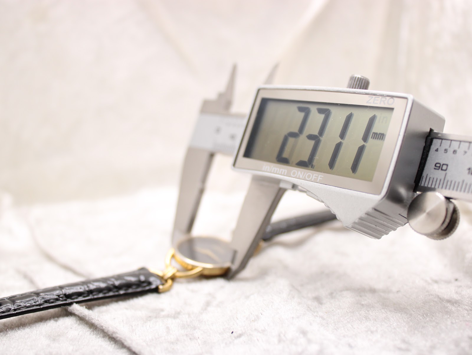 Digital caliper measuring the Gucci watch case diameter at 23.11 mm, showing the precise size of the gold-tone case.