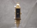 Front view of gold plated Gucci 1500L watch with black rectangular dial on a clear display stand.