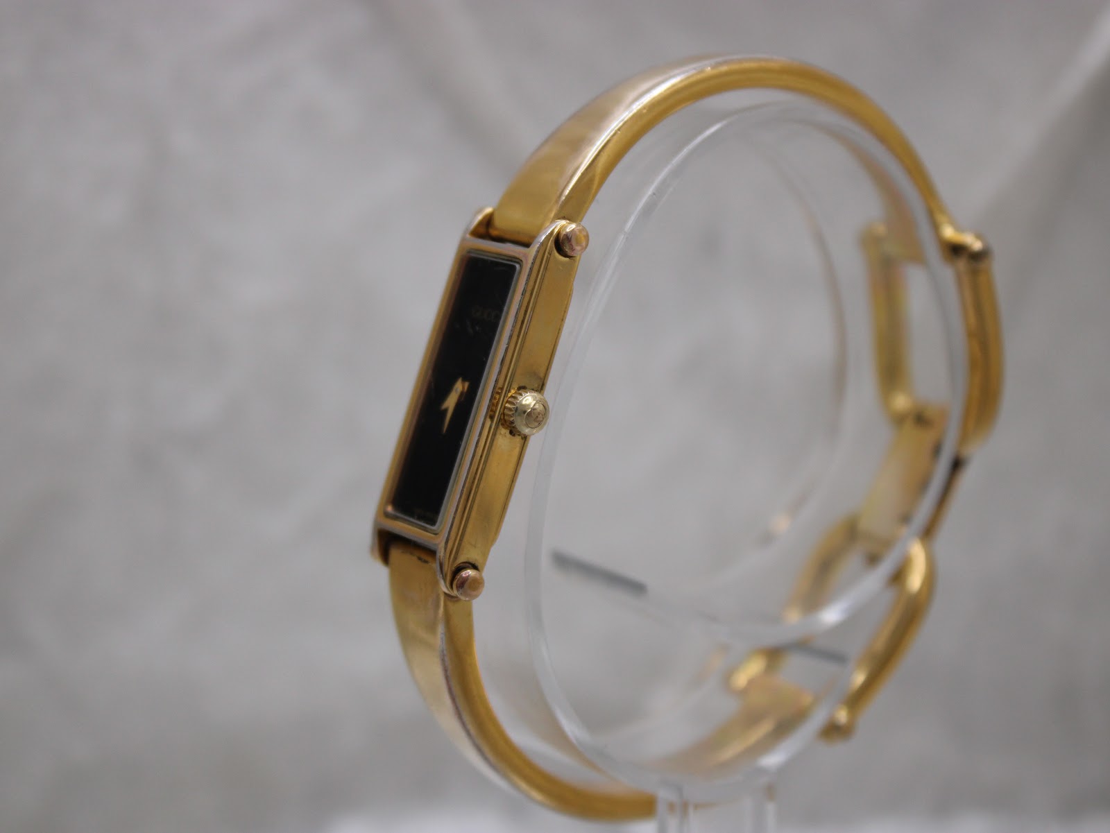 Angled side view of the gold plated Gucci 1500L watch on a clear display stand, showing the crown.
