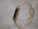 Angled side view of the gold plated Gucci 1500L watch on a clear display stand, showing the crown.