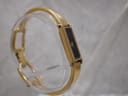 Another angled side view of the gold plated Gucci 1500L watch on a clear display stand, showing the full bangle shape.