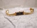 Top-down view of the gold plated Gucci 1500L bangle watch with clasp open, laid flat on a white textured surface.