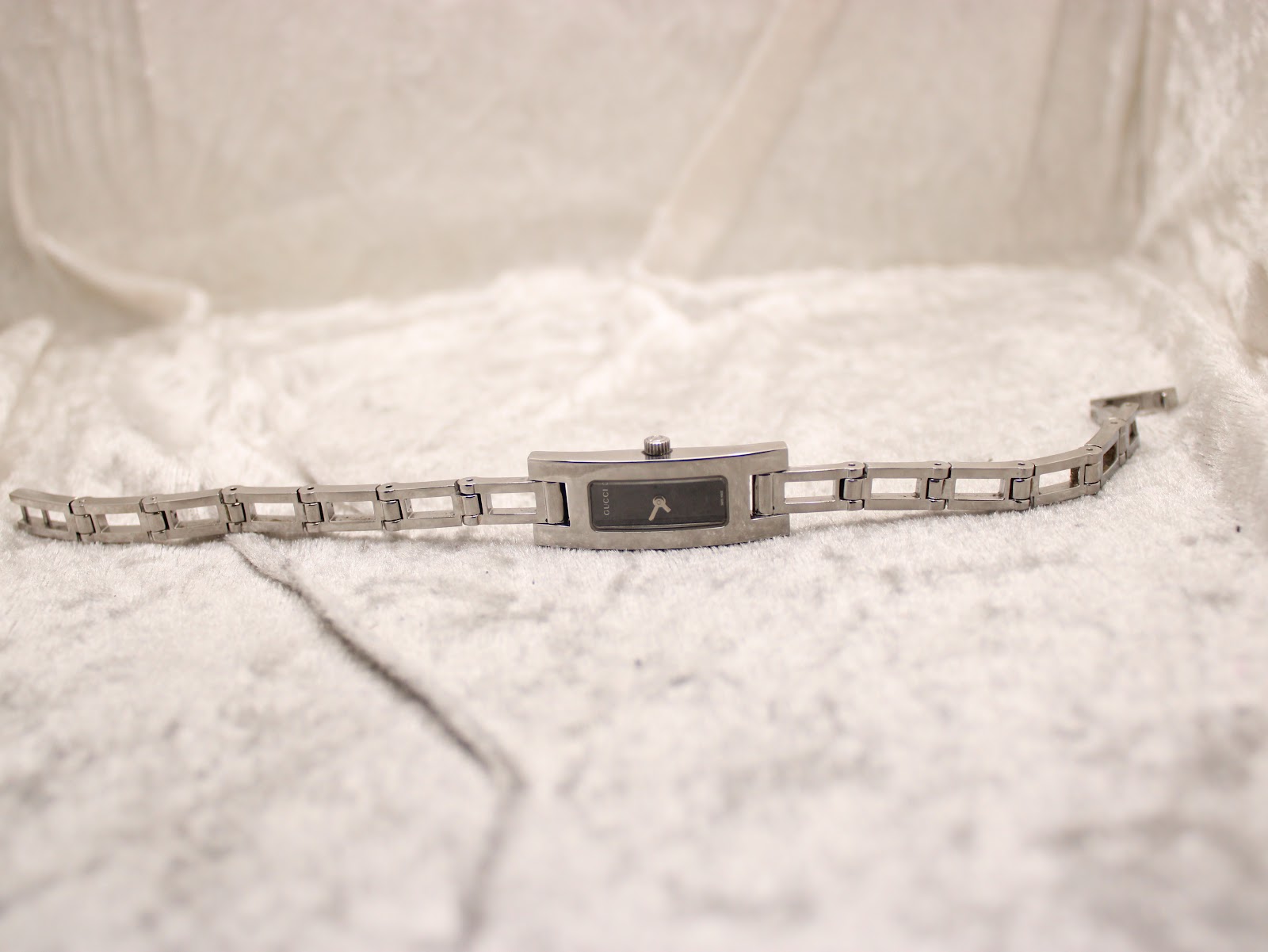 Full length view of the Gucci 3900L watch with its stainless steel bracelet laid flat on a white textured surface.
