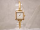 Front view of the gold-plated Gucci 1900L watch with a square white dial displayed on a clear stand.