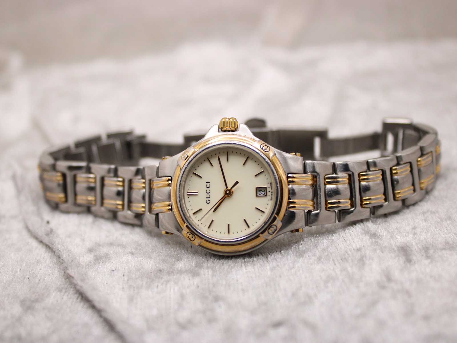 Front view of the Gucci 9040L watch laid flat on a textured white surface, displaying its two-tone bracelet extended.