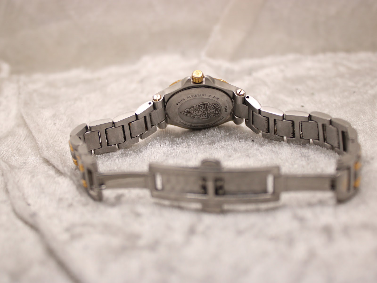 Back view of the Gucci 9040L watch with the bracelet open, showing the case back engraving and clasp interior on a textured white surface.