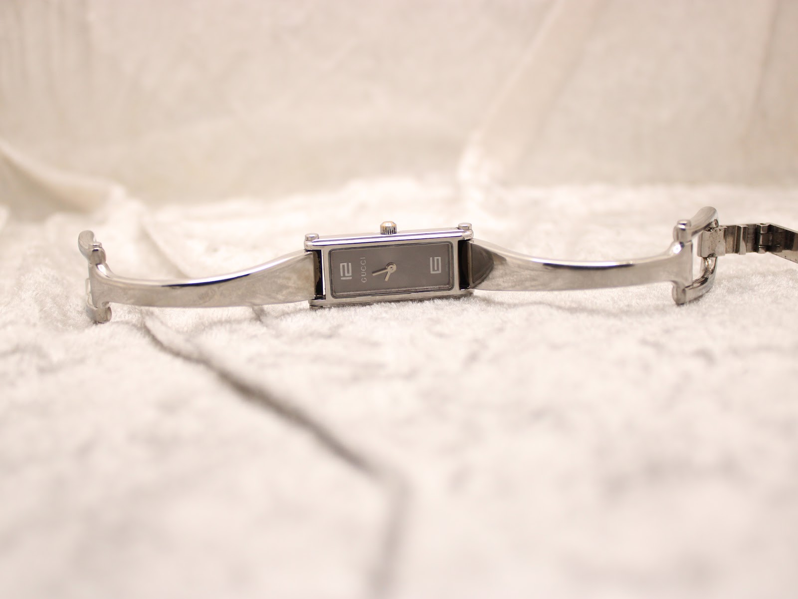 Full view of the Gucci 1500L watch with its bangle bracelet unclasped, laid flat on a textured white surface.