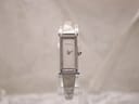 Front view of the Gucci 1500L watch on a clear display stand, showing the rectangular stainless steel case and white dial with silver hands.
