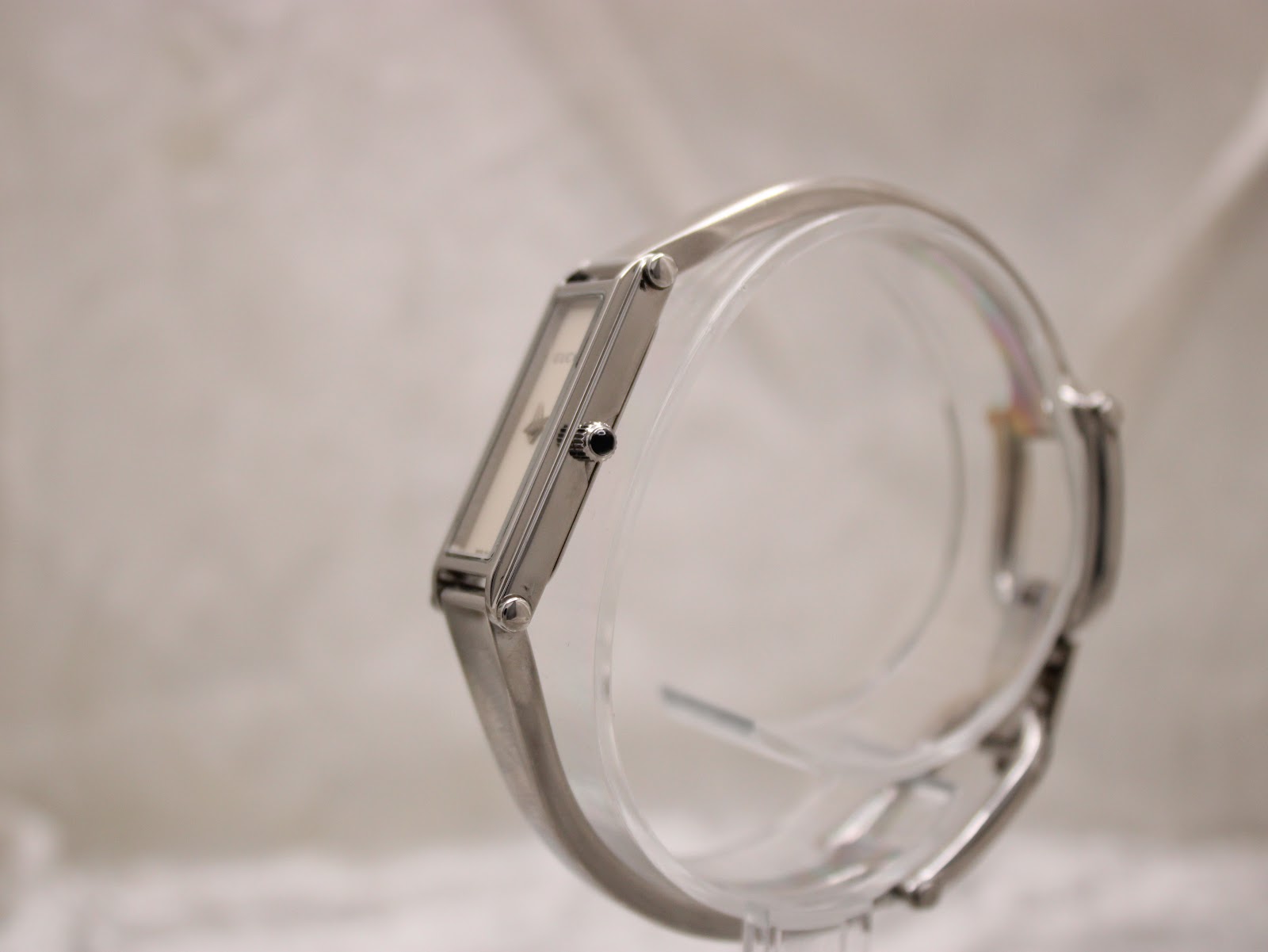 Side-angle view of the Gucci 1500L watch on a clear display stand, highlighting the slim profile and black cabochon crown.