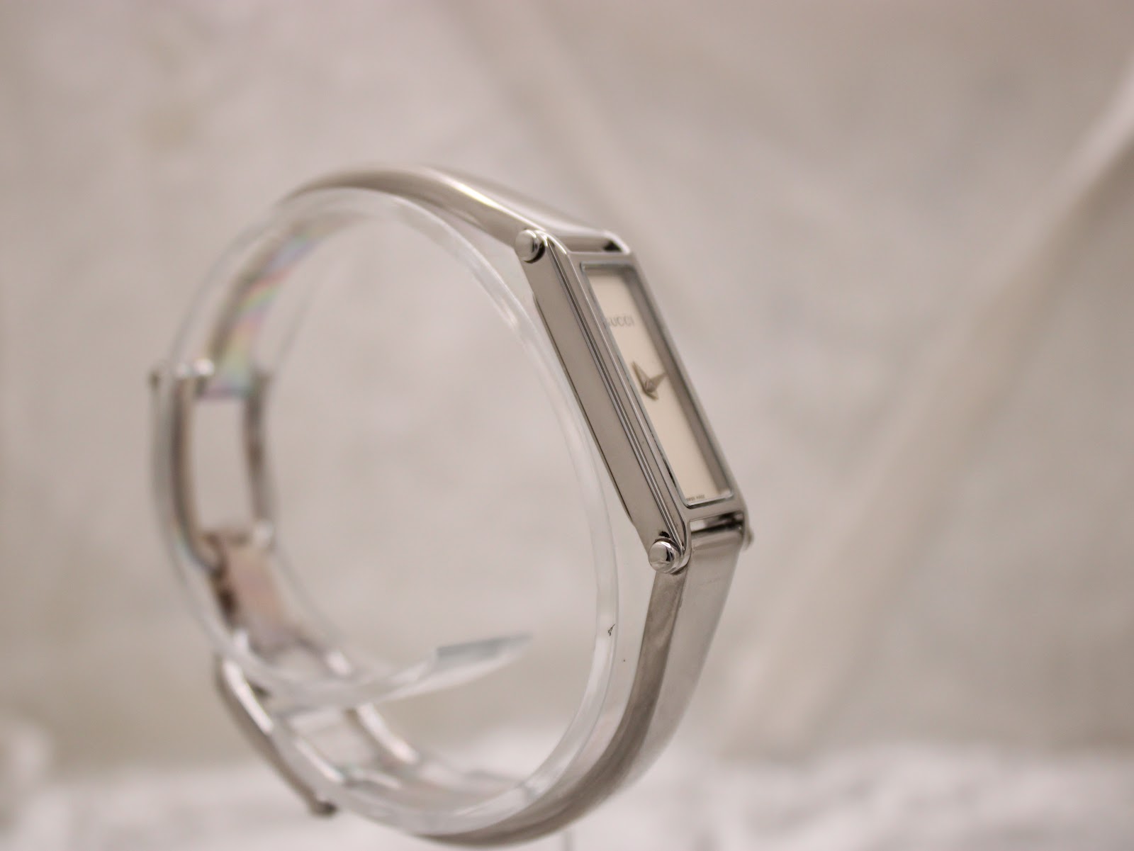 Another side-angle view of the Gucci 1500L watch on a clear display stand, showing the curvature of the bangle bracelet.
