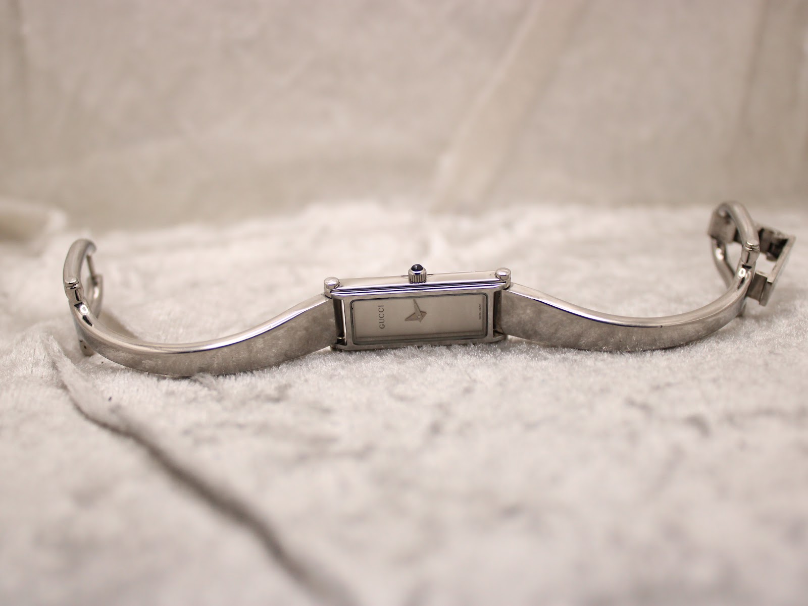 Top-down view of the opened Gucci 1500L bangle bracelet lying flat on a textured white surface, showing the full length.