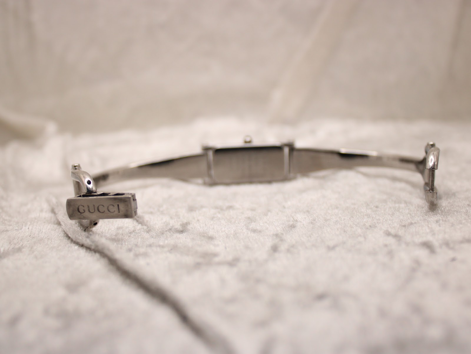 Close-up of the signed Gucci clasp on the bangle bracelet, with the watch body slightly out of focus in the background.