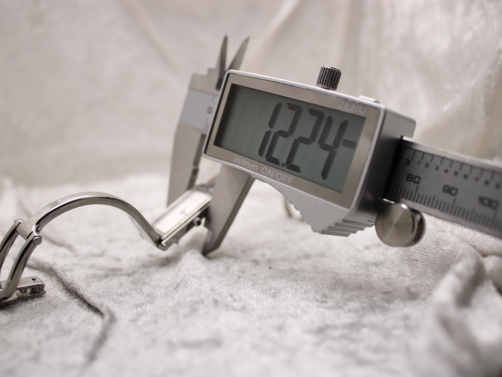 A digital caliper measuring the width of the Gucci 1500L watch case, displaying "12.24 mm".