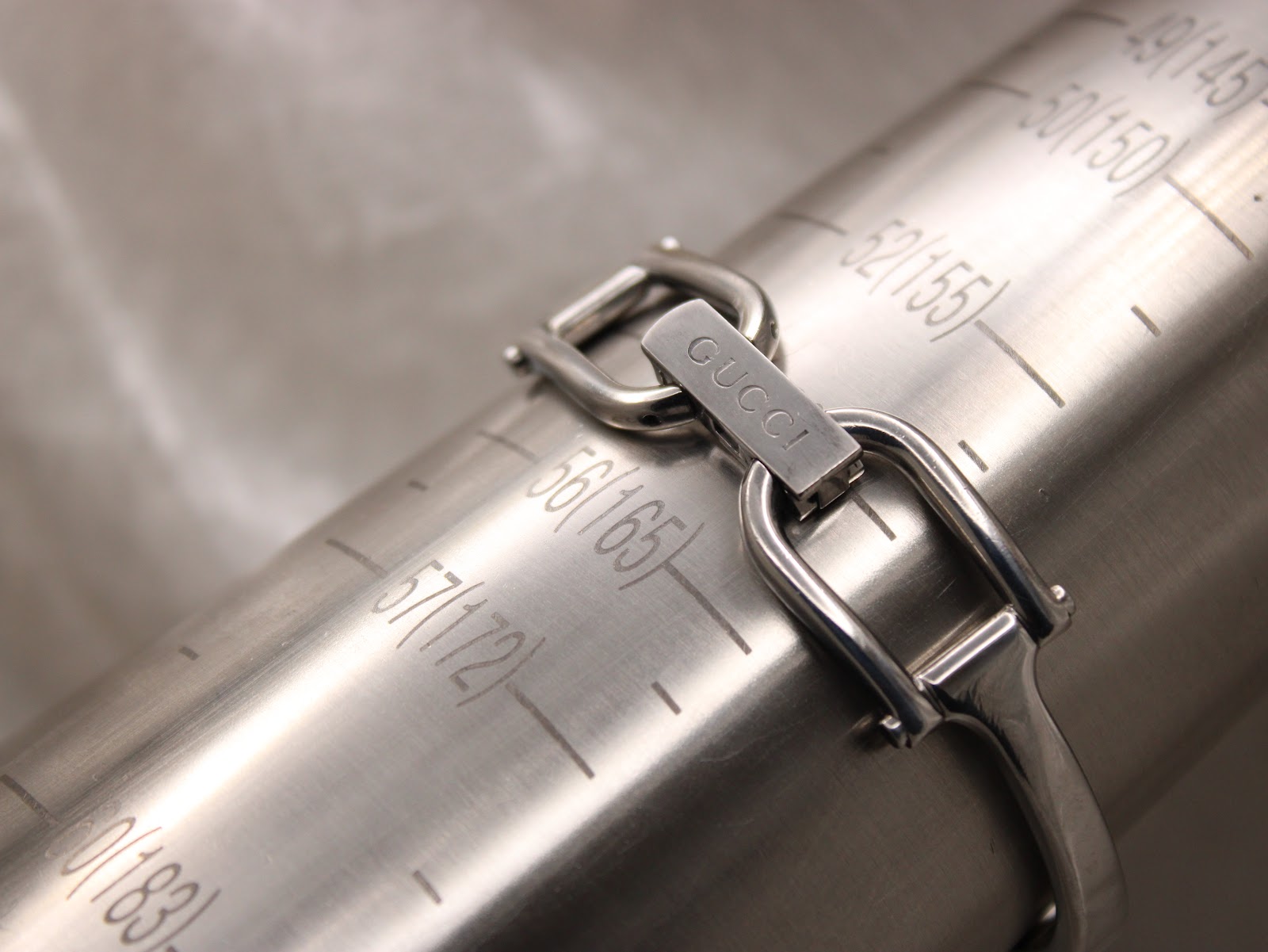 Close-up of the Gucci clasp on a metal wrist sizing gauge, showing a wrist fit of approximately 160mm or 16cm.
