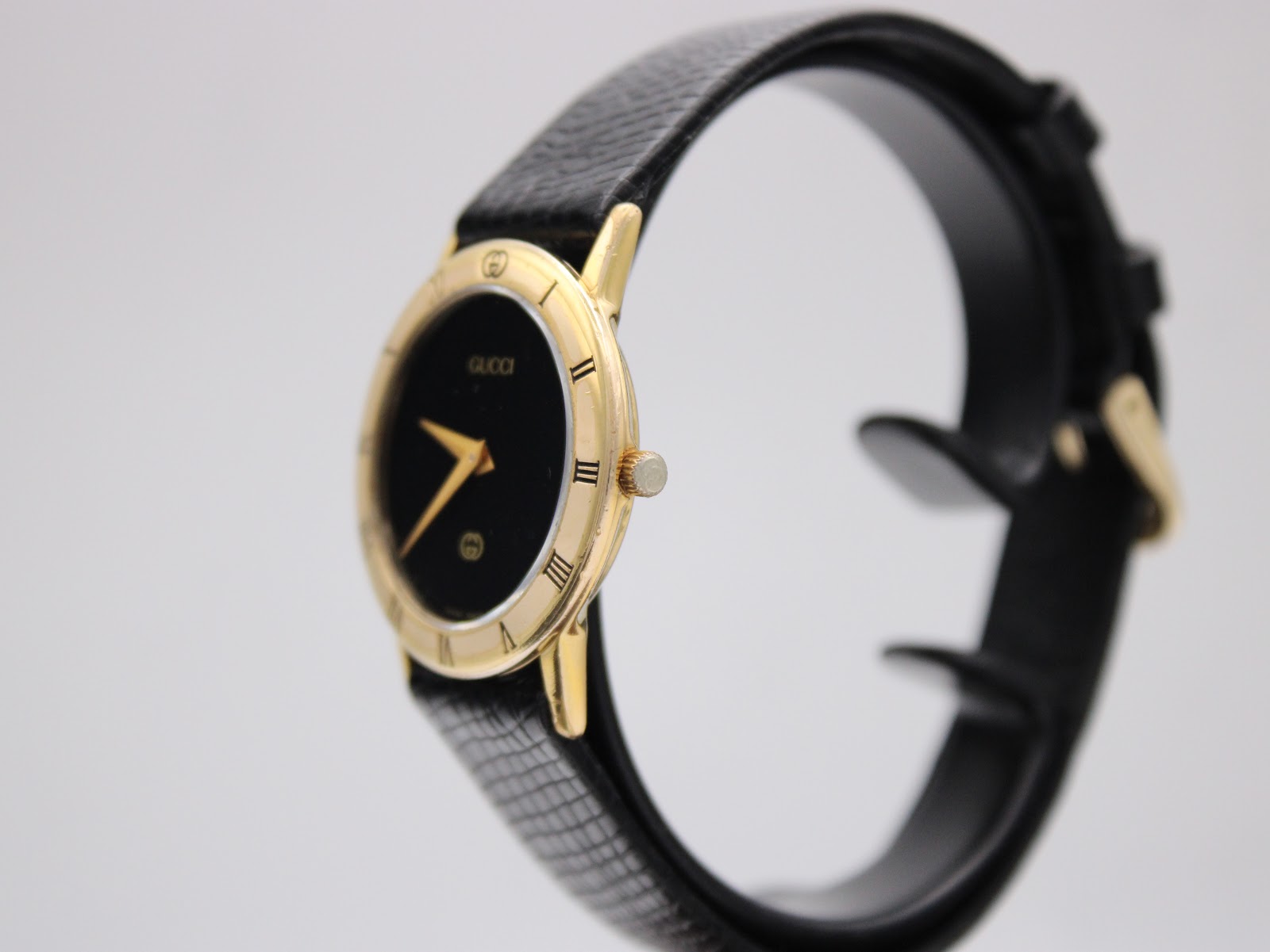 Right-side view of the gold-plated Gucci 3000 Jr watch on a display stand, showing the slim profile and crown.