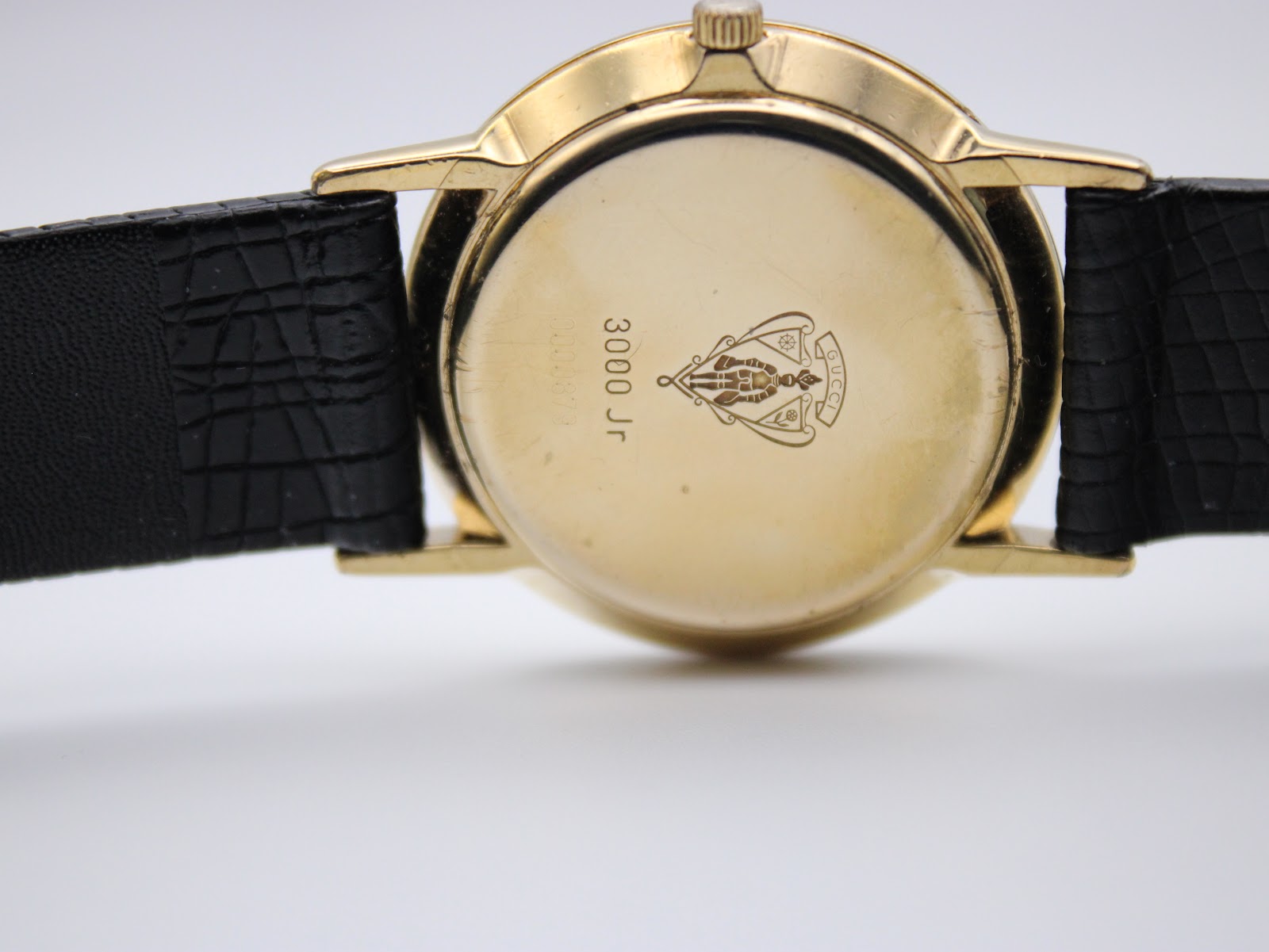 Close-up of the gold-plated case back of the Gucci 3000 Jr watch, showing Gucci crest and model engraving.
