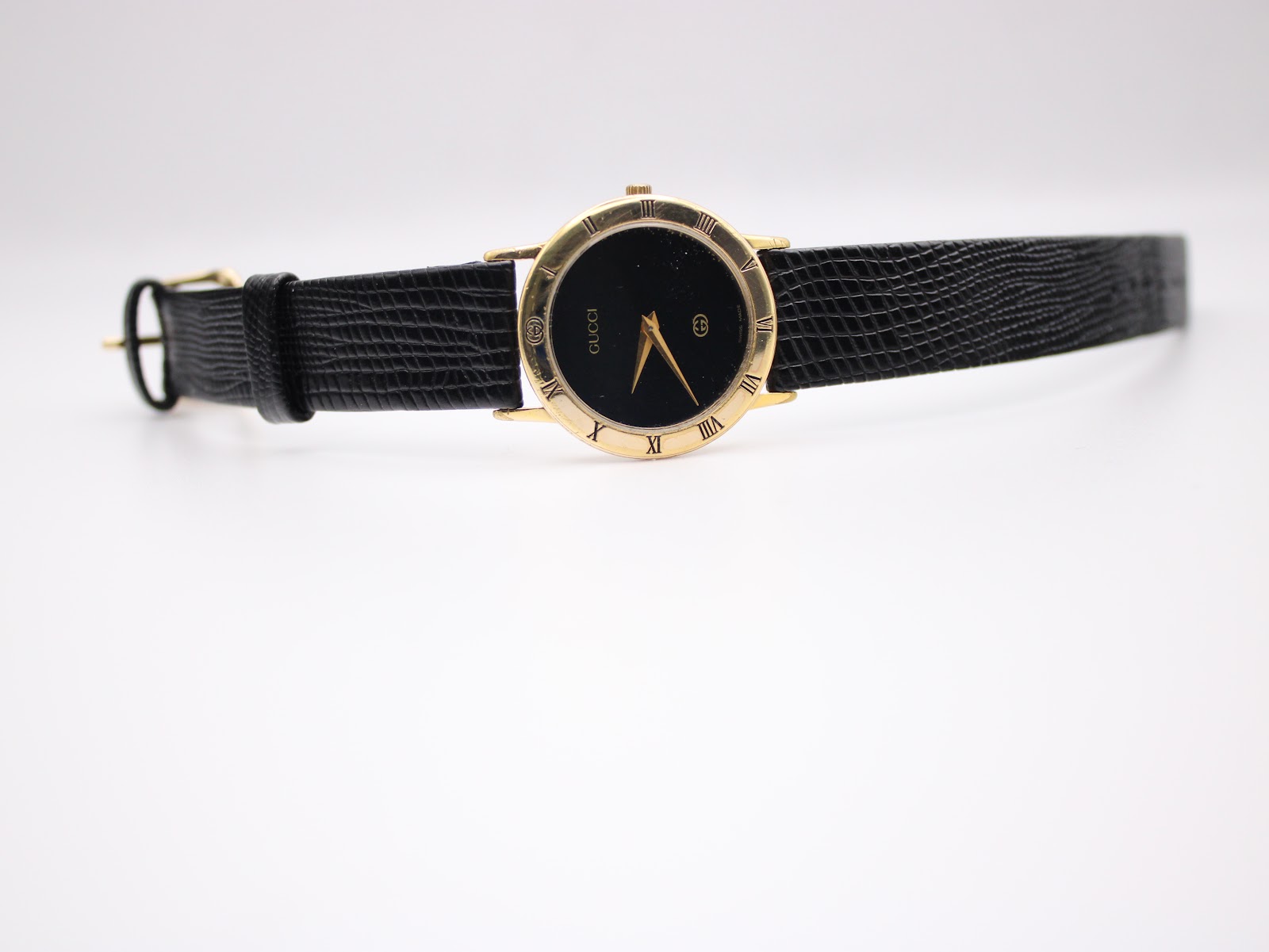 Frontal full view of the Gucci 3000 Jr watch, presenting the black dial, gold tone and textured black leather strap.