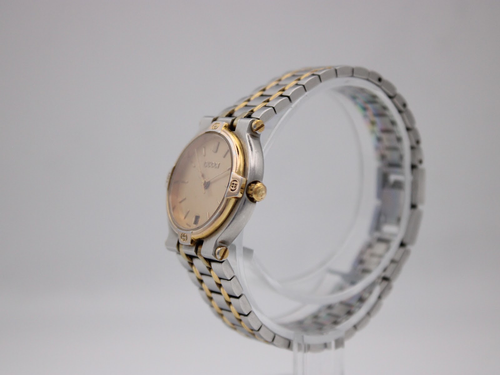 Side profile of the Gucci 9000 L watch, showcasing the gold-tone crown and the integrated bi-metal bracelet.