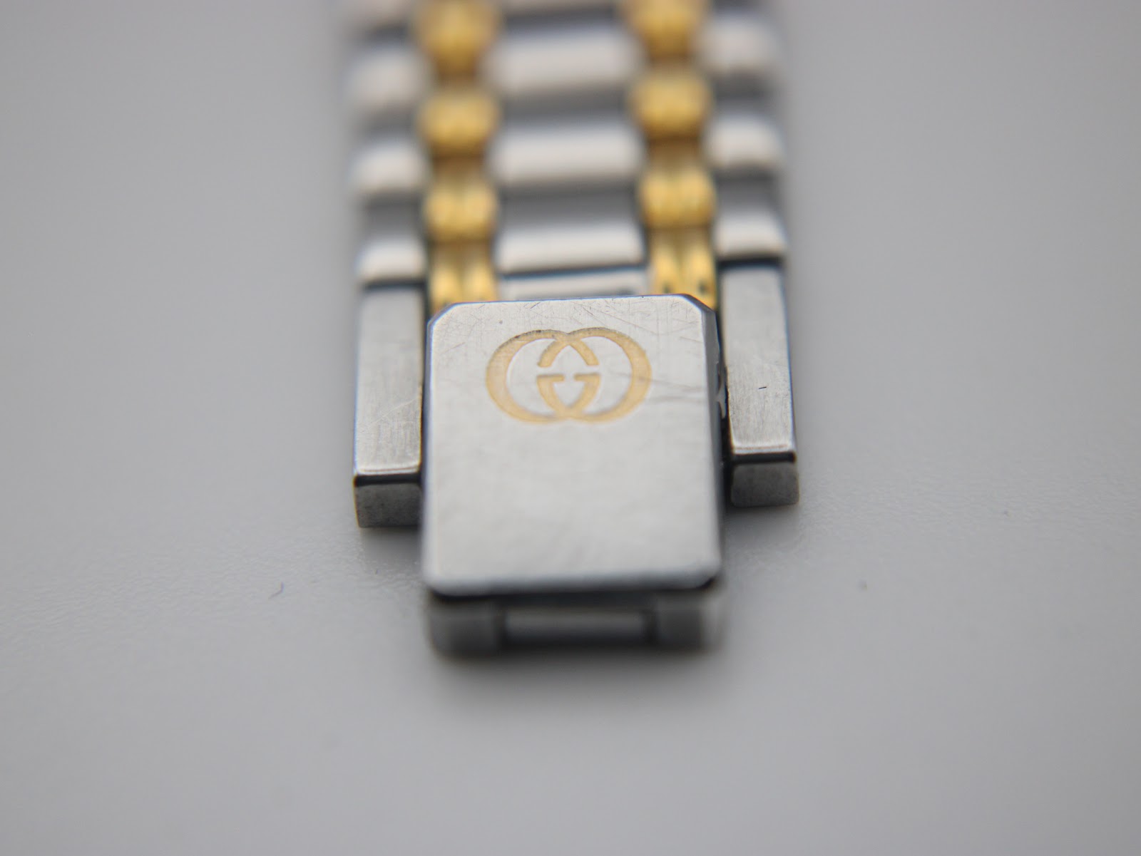 Macro shot of the bi-metal bracelet's fold-over clasp, clearly showing the iconic engraved Gucci interlocking G logo.