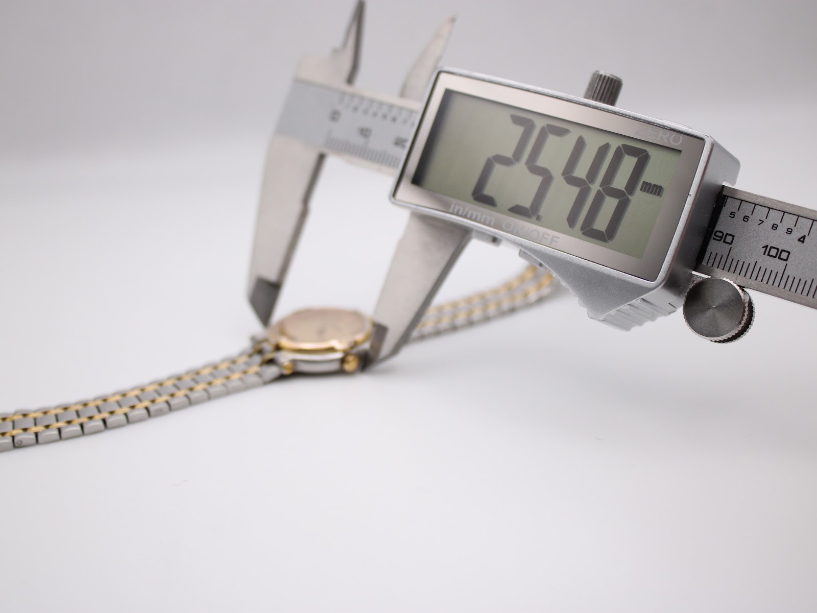 Digital caliper measuring the watch case diameter, displaying an exact measurement of 25.48 mm, with the bi-metal bracelet visible.