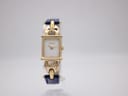 Front view of gold plated Gucci 1800 L watch with white dial and blue leather strap on a watch stand.