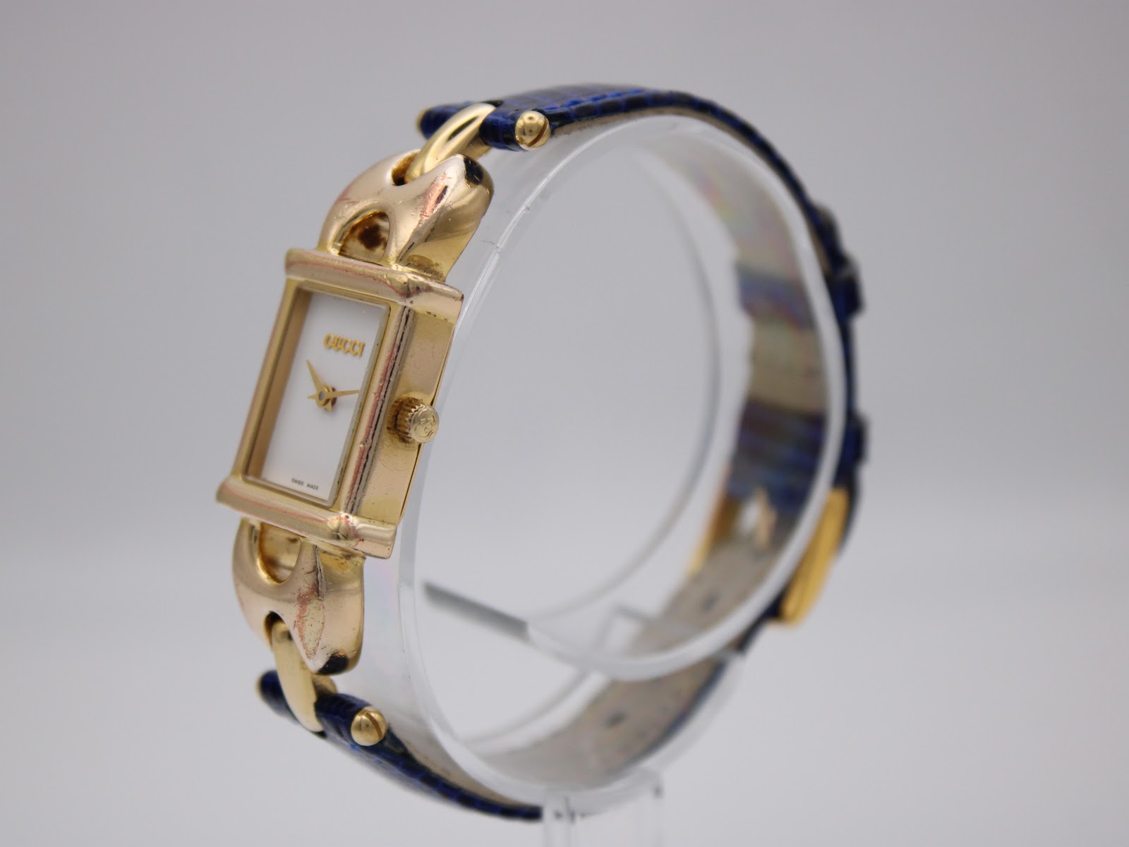 Angled view of the gold plated Gucci 1800 L watch, showing the right side of the rectangular case and blue leather strap.